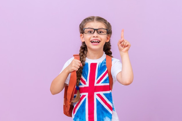 A schoolgirl with an image of the English flag on a T-shirt with glasses points her finger at the top. Learning English. isolated background.