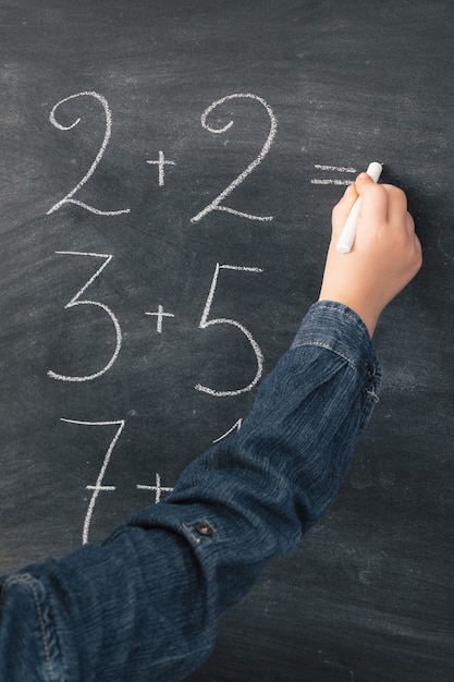 Schoolgirl writning math sums in chalk on blackboard