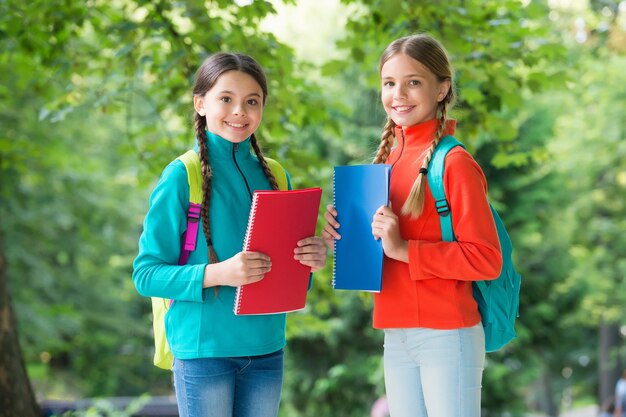 Schoolgirls with backpacks and textbooks in forest exploring nature concept