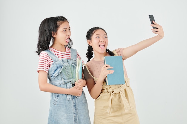 Schoolgirls with textbooks sticking out tongues when taking selfie after classes