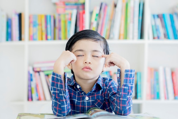 Schooljongen denken met gesloten ogen in bibliotheek