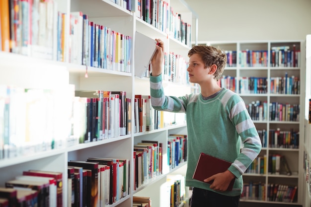 Schooljongen die boek in bibliotheek selecteert