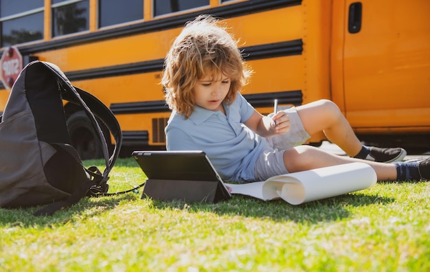 Schooljongen die buiten in het schoolpark schrijft en huiswerk doet op de schoolbus