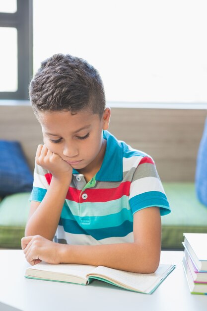 Schooljongen die een boek in bibliotheek leest