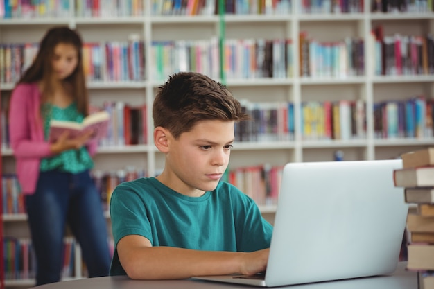 Schooljongen die laptop in bibliotheek op school met behulp van