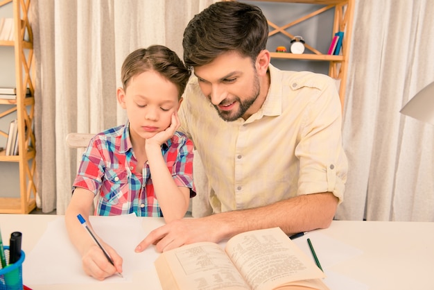 Schooljongen doet hometask met vader en schrijft in werkmap