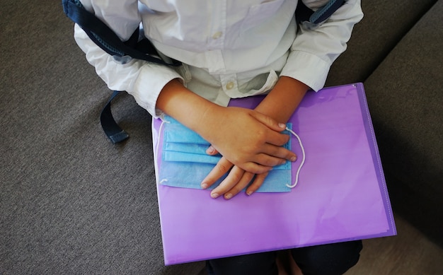 Schooljongen handen met map en medisch masker