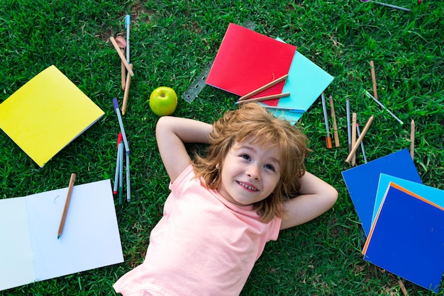 Schooljongen in de natuur voor de zomer ligt een kind in het gras droom over school studeren