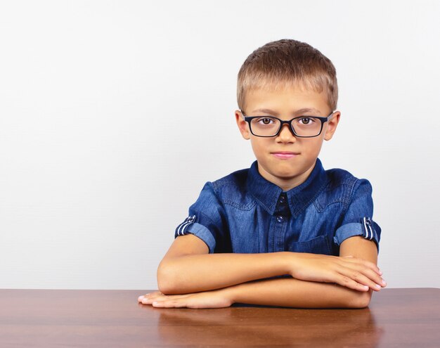 Schooljongen in een blauwe shirt zitten aan de tafel. Jongen met een bril