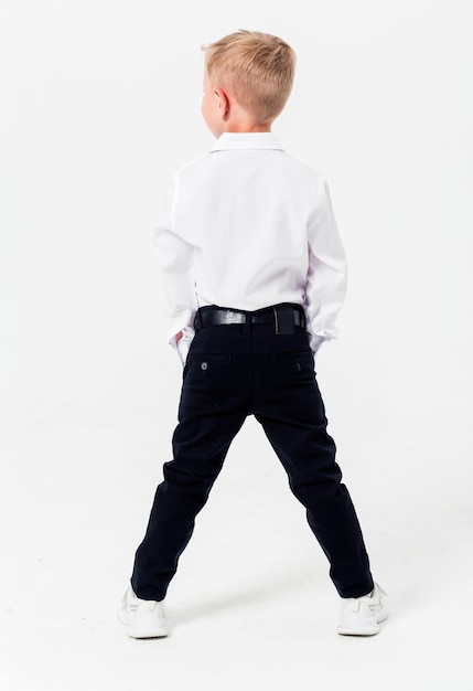 Schooljongen in een schooluniform op een witte achtergrond De jongen demonstreert een hemd, een broek, een riem en sneakers van achteren Verticale foto