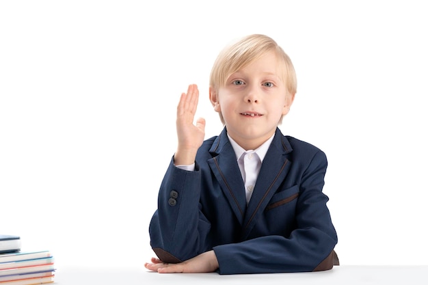 Schooljongen in schooluniform stak zijn hand hoog op om de vraag van de leraar te beantwoorden Portret van zevenjarige jongen geïsoleerd op een witte achtergrond