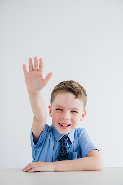 Schooljongen in schooluniform steekt zijn hand op aan de balie