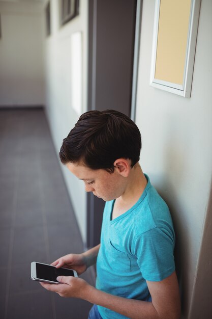 Schooljongen met behulp van mobiele telefoon in gang op school