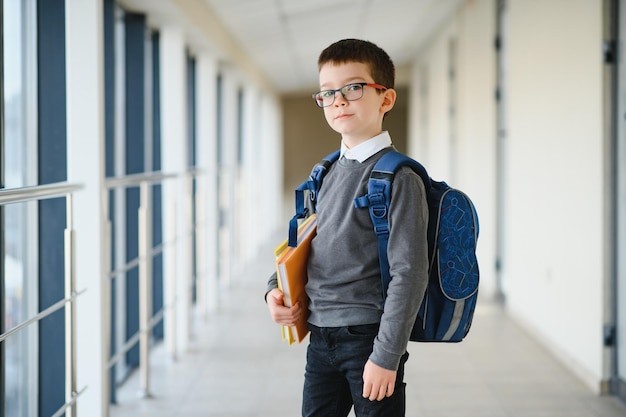 Schooljongen met schooltas en boeken in de school Onderwijsconcept Terug naar school Schoolkind gaat naar klas Stijlvolle jongen met rugzak Jongen klaar om te studeren