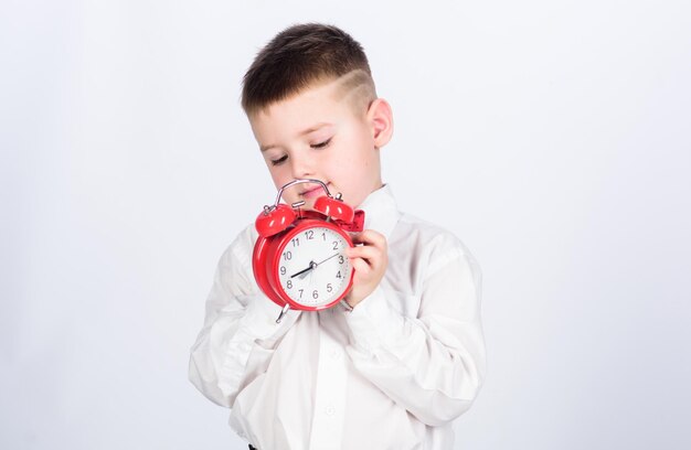 Schooljongen met wekker Kind schattige jongen wit overhemd rode vlinderdas Ontwikkel zelfdiscipline Stel wekker in Kind kleine jongen houdt rode klok vast Het is tijd Schema en timing Ochtendroutine