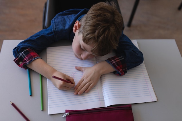 Schooljongen schrijft op een notitieboek en zit aan een bureau in de klas
