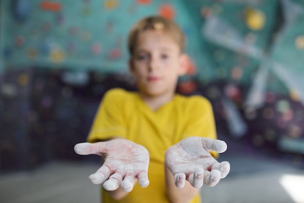 Schooljongen toont zijn handen bedekt met talk tijdens het klimmen in de sportschool