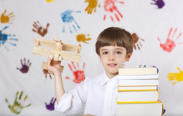 Schooljongen van 7 jaar oud gekleed in een overhemd, zittend aan tafel met een stapel woordenboeken