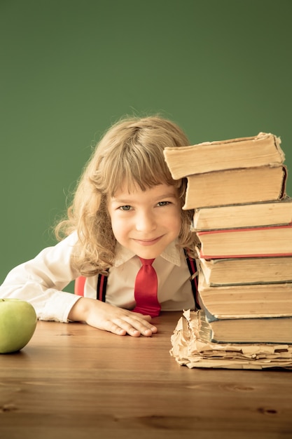 Schooljongen zit aan de balie in de klas. Gelukkig kind tegen groen bord. onderwijs concept