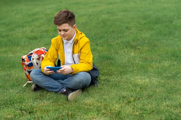 Schooljongen zit op het gazon met slimme telefoon