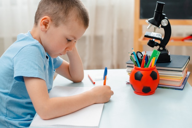 Schooljongen zitten thuis klaslokaal liggend bureau gevuld met boeken opleiding materiaal scholier