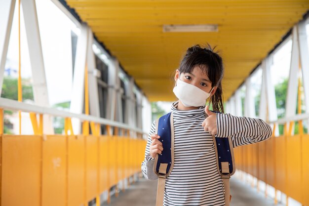 Schoolkind dat een gezichtsmasker draagt tijdens de uitbraak van het coronavirus Klein meisje gaat terug naar school