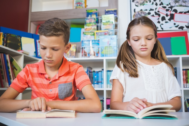 Schoolkinderen die boek in bibliotheek lezen