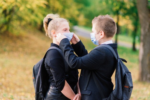 Schoolkinderen, een jongen en een meisje met medische maskers lopen in het stadspark.