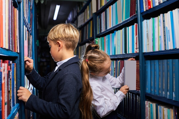 schoolkinderen in de bibliotheek die boeken kiezen die tussen de planken staan, terug naar elkaar, zich voorbereiden op school