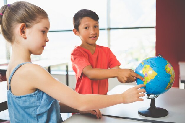 Schoolkinderen kijken naar globe in de klas