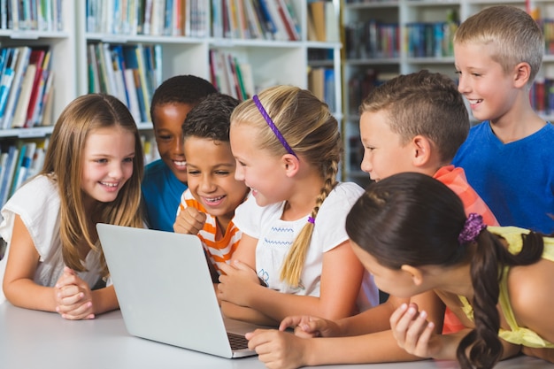 Schoolkinderen met behulp van laptop in bibliotheek