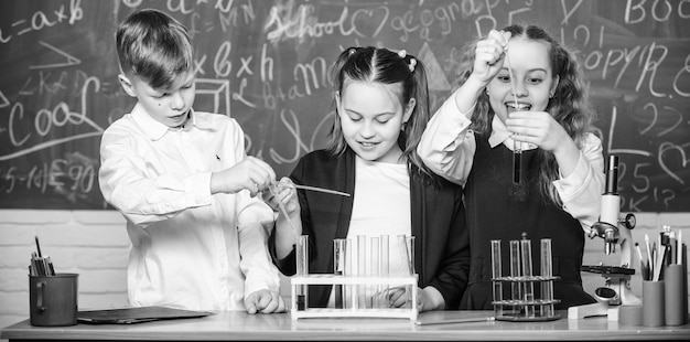 Foto schoollaboratorium meisjes en jongen die experimenteren met vloeistoffen reageerbuisjes met kleurrijke vloeibare stoffen studie van vloeibare toestanden groepsschoolleerlingen met reageerbuisjes bestuderen chemische vloeistoffen