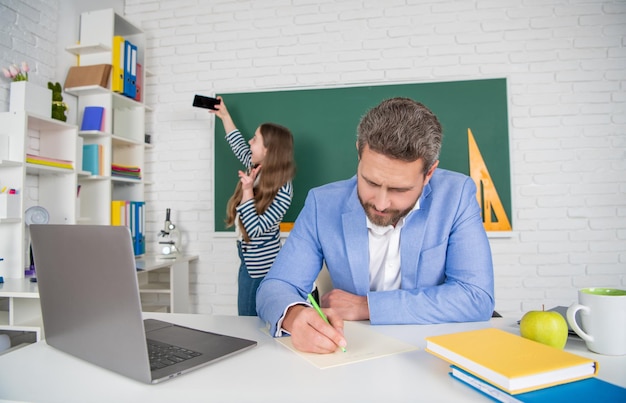 Schoolleraar in de klas met selectieve focus van kind dat selfie maakt op blackboard