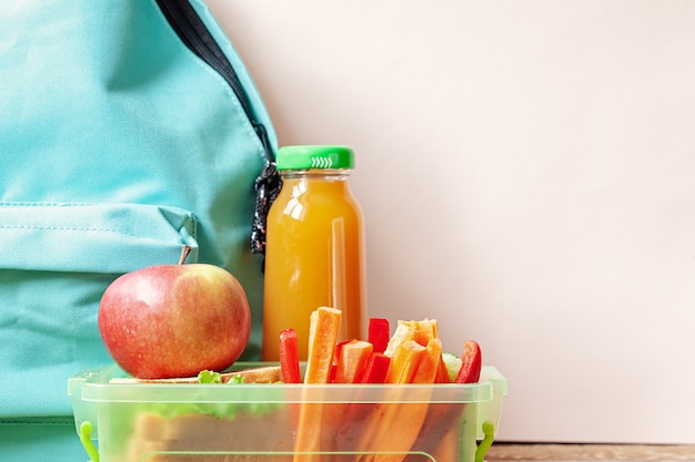 Schoollunchdoos met sandwich, groenten, sap en amandelen op lijst.