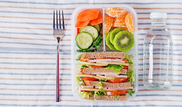 Schoolmaaltijd vak met sandwich, groenten, water en fruit op tafel. Gezonde eetgewoonten concept. Plat leggen. Bovenaanzicht