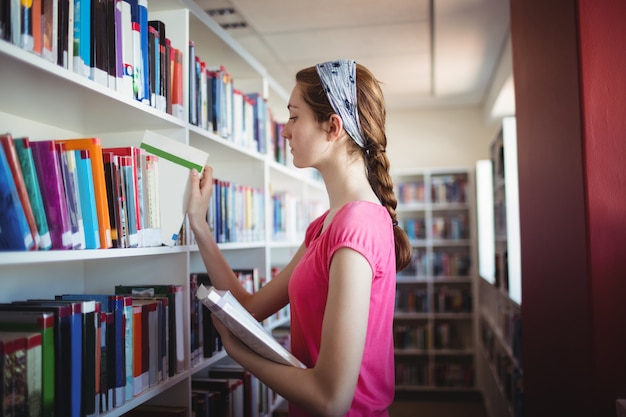 Schoolmeisje boek selecteren uit boekenplank in bibliotheek