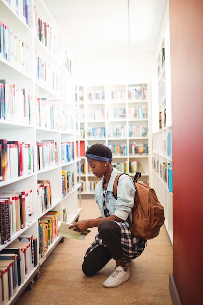 Schoolmeisje boek selecteren uit boekenplank in bibliotheek