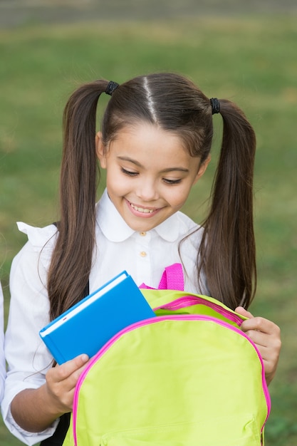 Schoolmeisje dat boek in rugzak zet, klaar voor lessenconcept