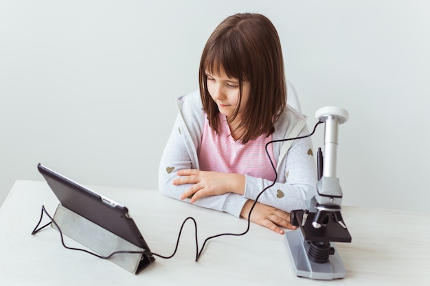 Schoolmeisje die microscoop in wetenschapsklasse gebruiken. Technologieën, lessen en kinderen concept.