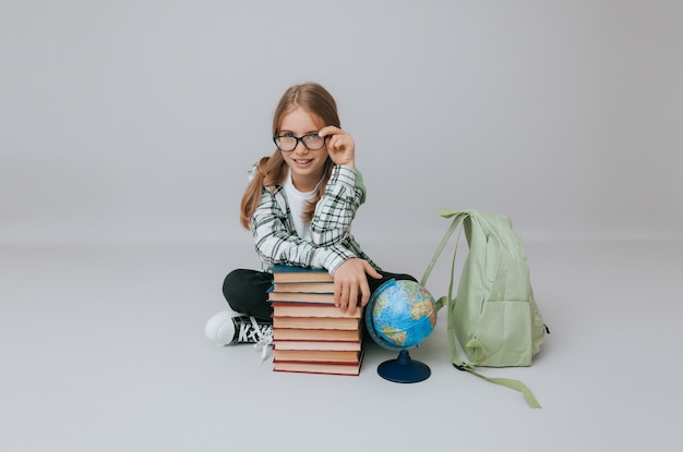 Schoolmeisje geïsoleerd op gele achtergrond met globe meisje in schooluniform zittend op een gele achtergrond lezen van een boek blond meisje in schooluniform op een gele achtergrond