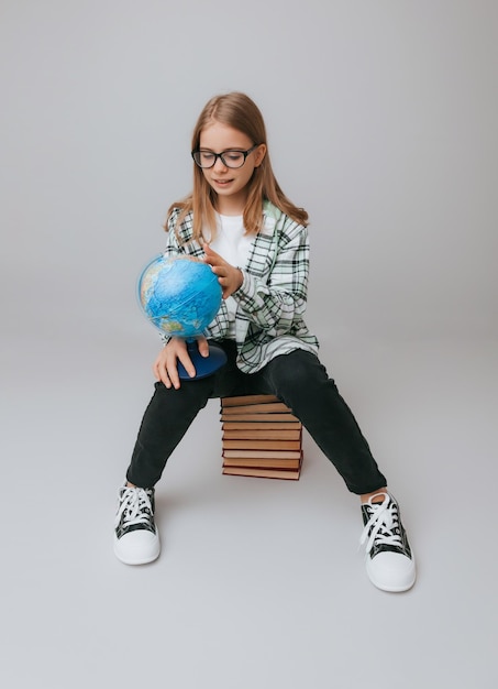 Schoolmeisje geïsoleerd op gele achtergrond met globe meisje in schooluniform zittend op een gele achtergrond lezen van een boek blond meisje in schooluniform op een gele achtergrond