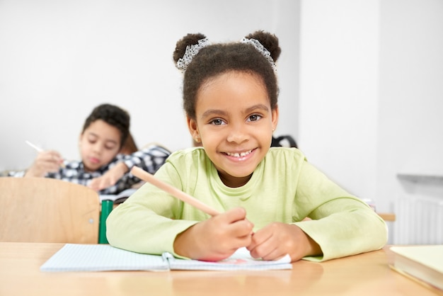 Schoolmeisje glimlachen, die in klaslokaal op basisschool stellen.