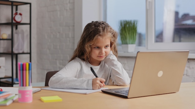 Schoolmeisje heeft online les, schrijft in werkboek, maakt huiswerk. Afstand leren.