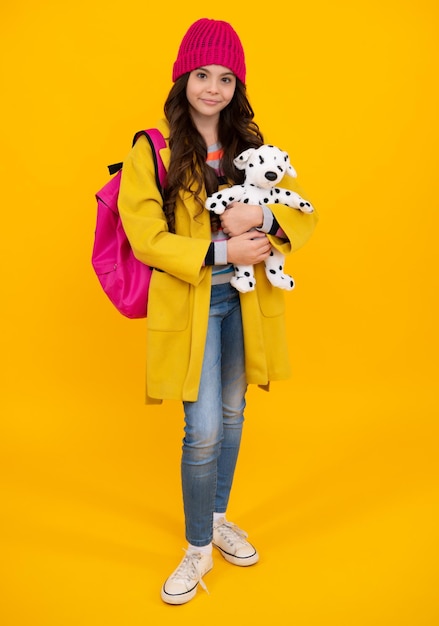 Schoolmeisje houdt speelgoed vast Schoolkinderen met favoriet speelgoed op gele geïsoleerde achtergrond Jeugdconcept