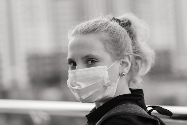 Schoolmeisje in beschermend medisch masker bij zonsondergang. moderne leerling met rugzak tijdens de covid-19 quarantaine.