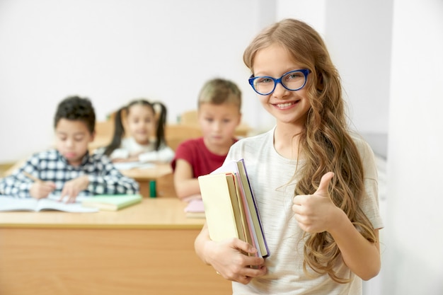 Schoolmeisje in de klas bedrijf boeken, duim opdagen.