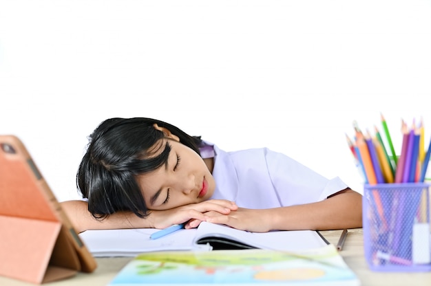 Schoolmeisje in een uniforme vergadering Slapen op de tafel in de buurt van tablet en boek, concept voor leunen of examen met online e-learning leraar en drowse of studeer hard