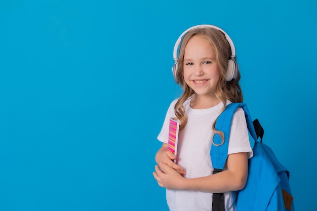 schoolmeisje in een wit T-shirt, koptelefoon, met een rugzak op haar schouder en een gestreept notitieboekje