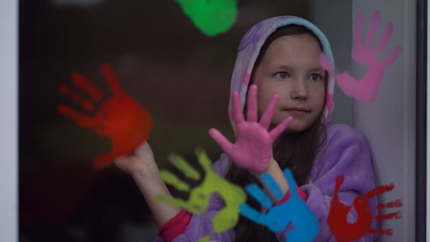 Foto schoolmeisje in pyjama's schilderen met palmen op het raam. quarantaine blijf thuis