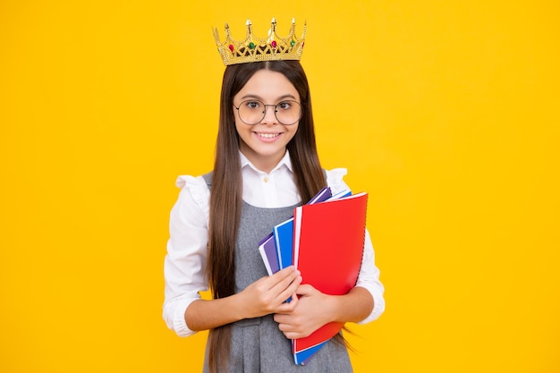 Schoolmeisje in schooluniform en kroon vieren overwinning op gele achtergrond School kind hold